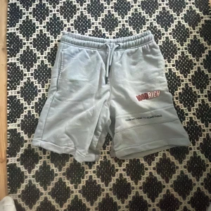 Grå shorts från Hoodrich - Säljer ett par grå shorts från Hoodrich med elastisk midja och snörning. De har en cool textdetalj på sidan och är perfekta för en avslappnad stil. Passar ungdomar som är 148-158 
