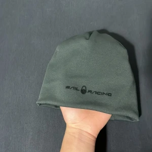 Mörk grön från Sail Racing - Snygg grön mössa från Sail Racing, perfekt för kyliga dagar. Tillverkad av 96% återvunnen polyester och 4% polyuretan. Diskret logga framtill ger en stilren look.
