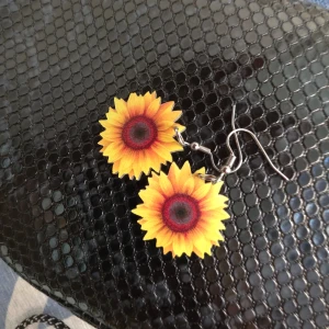 Solrosformade örhängen - Säljer ett par färgglada örhängen i form av solrosor. De har en härlig gul färg med en mörkare mitt och är perfekta för att lysa upp vilken outfit som helst. Örhängena har en enkel krok för att enkelt sätta i och ta ur.