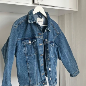 Blå jeansjacka från Monki - Säljer en klassisk blå jeansjacka från Monki i storlek XS. Jackan har en normal passform med knappar framtill och två bröstfickor. Perfekt för vår och sommar!