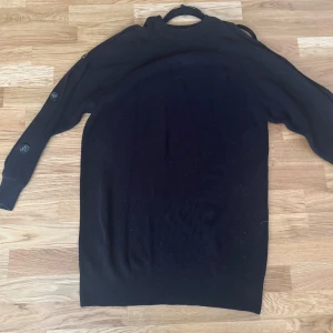 Svart stickad kofta med knappar - Snygg svart stickad kofta med knappar längs ärmarna. Perfekt för kyliga dagar och enkel att matcha med olika outfits. Saknar en knapp på ena armen 