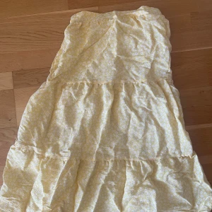 Gul blommig kjol - Söt gul kjol med vita blommor i storlek 34. Den har resår i midjan för bekväm passform och är vadlång. Säljer pga för liten storlek.