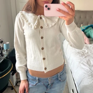 Vit kofta! - Säljer en söt vit kofta med volangkrage och knappar framtill. Perfekt för en stilren och elegant look. Passar bra till både jeans och kjol.