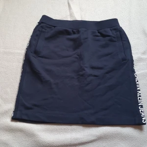 Svart kjol från Calvin Klein Jeans - Svart kjol från Calvin Klein Jeans med elastisk midja och fickor. Kjolen har en sportig look med logotypen tryckt längs sidorna. Storlek XS men stretchig 🌟