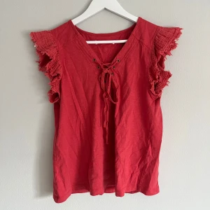 Röd topp med volangärmar och snörning - Snygg röd topp med volangärmar och dekorativ snörning framtill. Perfekt för en somrig look med en touch av bohemisk stil.