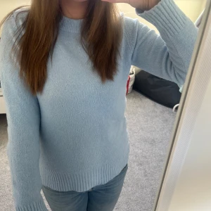 Ljusblå stickad tröja - Säljer en ljusblå stickad tröja med långa ärmar och ribbade muddar vid ärmslut och nederkant. Perfekt för kyligare dagar och ger en mysig känsla. Passar bra till jeans eller kjol för en avslappnad look.