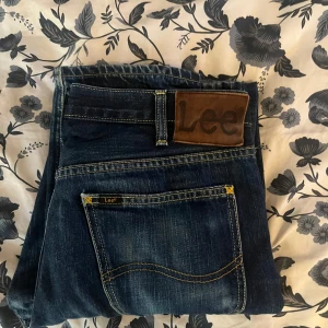Mörkblå jeans från Lee - Snygga mörkblå jeans från Lee med klassisk femficksdesign och en läderpatch med logga på baksidan. Jeansen har en straight passform och är perfekta för en avslappnad stil. De har en lätt tvättad look som ger en cool touch.