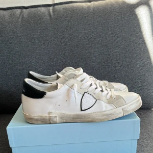 Vita sneakers från Philippe Model - Snygga vita sneakers från Philippe Model med svarta detaljer och snörning. Skorna har en rund tå och är tillverkade i skinn med en stilren design perfekt till sommaren. Små tecken på användning men använd väldigt sparsamt. Box och dustbag följer såklart med. Tveka inte vid funderingar!😁Trades funkar också. 