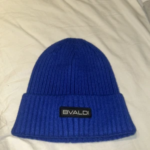 Blå beanie mössa från BVALDI - Snygg blå ribbad mössa från BVALDI med en stilren logga framtill. Perfekt för att hålla värmen under kyliga dagar. Enkel och stilren design som passar till det mesta.