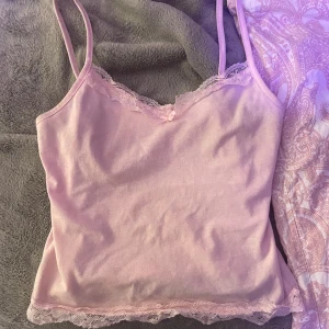 Rosa linnetopp med spetsdetaljer - Söt rosa linnetopp med smala axelband och spetsdetaljer vid halsringning och nederkant. Perfekt för varma dagar eller som ett lager under en tröja.