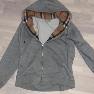 Grå hoodie från Burberry - Säljer en stilren grå zip hoodie från Burberry. Den är xl men passar L