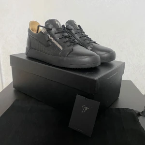 Giuseppe Zanotti - Snygga svarta sneakers från Giuseppe Zanotti med dragkedja och snörning. Skorna har en unik design med krokodilmönstrade detaljer på sidorna och en blixtlogga på plösen.