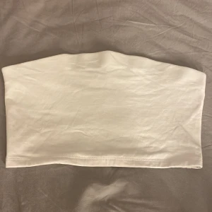 Vit tubtopp - Säljer en enkel och stilren vit tubtopp. Perfekt för varma sommardagar eller som basplagg under en kavaj. Tillverkad i mjukt och bekvämt material.