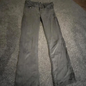 Grå byxor från Gina Tricot - Snygga grå byxor från Gina Tricot med raka ben och knappdetaljer. Perfekta för en stilren look. Byxorna har en klassisk design med fickor bak och fram.