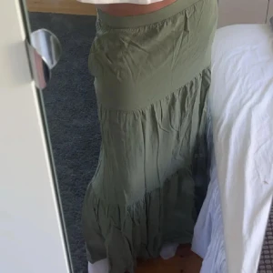 Grön långkjol - Säljer en snygg grön långkjol med knytband i midjan. Kjolen har en avslappnad passform och är perfekt för varma dagar. Den är gjord i ett lätt och luftigt material som ger en skön känsla.💕💕