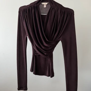 Burgundy omlottopp - Elegant burgundy omlottopp med långa ärmar och draperad design. Perfekt för en stilren look. Använd 1 gång 