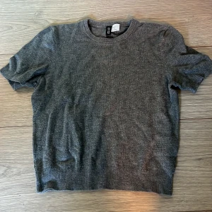 Grå kortärmad tröja från H&M Divided - Säljer en stilren grå kortärmad tröja från H&M Divided. Perfekt för en avslappnad look. Tröjan har en rund halsringning och ribbade kanter vid ärmslut och nederkant.