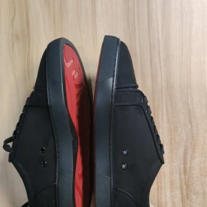 Svarta christian louboutin skor  - Snygga svarta christian louboutin sneakers med en ikonisk röd sula. Skorna har snörning och en stilren design som passar perfekt för en trendig look. Insidan är ljus med en elegant guldfärgad logotyp.