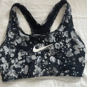 Svart och vit sporttopp från Nike - Säljer en snygg sporttopp från Nike i svart och vitt med ett abstrakt mönster. Toppen har en brottarrygg och är tillverkad i Dri-FIT-material för optimal komfort under träning. Perfekt för gymmet eller löprundan! Säljer även en helsvart och om du är interisserad kan du köpa båda för 100kr 