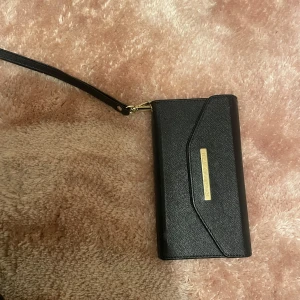 Svart plånboks skal med handledsrem - Elegant svart plånbok/ iPhone 6 skal med en praktisk handledsrem och gulddetaljer. Plånboken har flera kortfack och en magnetisk stängning. Perfekt för att hålla dina kort och kontanter organiserade.