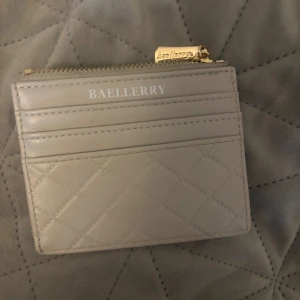 Grå plånbok från Baellerry - Säljer en stilren grå plånbok från Baellerry med quiltad design och dragkedja. Plånboken har flera kortfack och ett fönsterfack på baksidan för ID eller foto. Perfekt för att hålla ordning på dina kort och kontanter.
