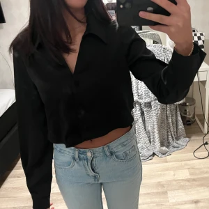 Svart croppad skjorta - Snygg svart croppad skjorta med långa ärmar och knappar framtill från Zara . Perfekt för en stilren look. Passar bra till jeans eller kjol.