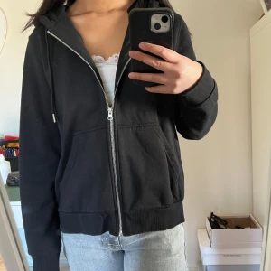 Svart hoodie med dragkedja - Säljer en svart hoodie med dragkedja och huva. Den har långa ärmar och ribbade muddar vid ärmslut och nederkant. Aldrig använd, men tog tyvärr bort prislappen