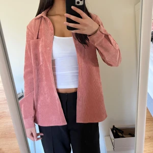 Rosa manchester overshirt - Säljer en snygg rosa manchester overshirt med knappar framtill. Skjortan har en avslappnad passform och en bröstficka. Perfekt för lager-på-lager-stil.