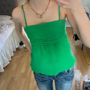 Grön topp från GAP - Snygg grön linnetopp från GAP med smala axelband och rynkad detalj framtill. Perfekt för sommardagar och kan enkelt matchas med jeans eller kjol. 💚