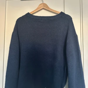 Mörkblå stickad tröja - Säljer en mysig mörkblå stickad tröja med rund hals. Perfekt för kyliga dagar och enkel att matcha med olika outfits. Tröjan har långa ärmar och en avslappnad passform.