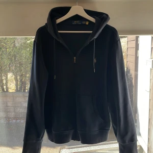 Ralph lauren zip hoddie - Säljer en stilren svart hoodie från Polo Ralph Lauren med dragkedja och justerbar huva. Tröjan har långa ärmar och en liten logotyp på bröstet. Perfekt för en avslappnad look.