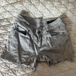 Grå lågmidjande  jeansshorts från Stockh LM - Snygga grå jeansshorts från Stockh LM med slitna detaljer och fransig kant. Perfekta för en avslappnad stil. De har en klassisk femficksdesign och knappgylf.