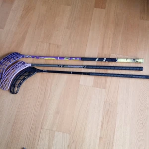 Innebandyklubbor i olika färger - Tre innebandyklubbor med olika färger och mönster. En har ett lila blad och svart skaft, en annan har ett svart blad och skaft med vita detaljer, och den tredje har ett lila blad med ett färgglatt skaft. Perfekt för innebandyentusiaster som vill ha variation i sitt spel. Om man vill köpa alla klubbor så vill jag ha 1000 men om man köpa en klubba 400 kr för vajer klubba om man vill veta hur lång klubborna så får ni skriver till mig 