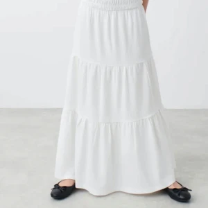 Vit långkjol från Gina tricot - Säljer en elegant vit långkjol med volanger. Kjolen har en luftig och flödande design som är perfekt för varma dagar och somriga kvällar. Stl 158