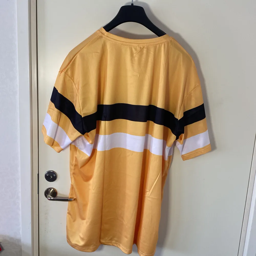 Helt ny . Snygg gul t-shirt från Fred Perry med svarta och vita ränder över bröstet. Den har en normal passform och korta ärmar, perfekt för en avslappnad stil. Den ikoniska Fred Perry-loggan är broderad på bröstet.. T-paidat.