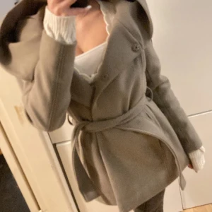 Beige kappa med luva  - Snygg beige kappa från Zara med knappar och bälte i midjan. Den har en stor krage och är perfekt för kyligare dagar. Kappan är stilren och passar till många olika outfits.