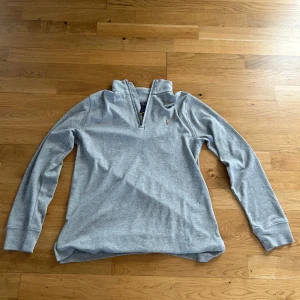Grå tröja från Ralph Lauren (pris kan diskuteras) - Säljer en stilren grå tröja från Ralph Lauren med dragkedja och broderad logga på bröstet. Perfekt för en avslappnad och snygg look. Tröjan har långa ärmar och en bekväm passform. Storlek 156-164 och köpt på kidsbrandstore för 1100 kr. Nästan helt oanvänd så därför priset 700