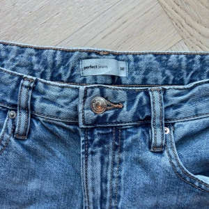 Blå jeans från Gina Tricot - Säljer ett par klassiska blå jeans från Gina Tricot. De har en rak passform och är tillverkade i denim med en knapp och dragkedja framtill. Perfekta för en avslappnad stil.