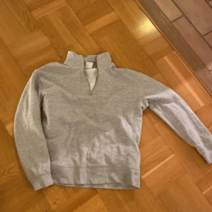 Grå tröja med dragkedja från Zara - Säljer en stilren grå tröja från Zara med halv dragkedja vid halsen. Tröjan har långa ärmar och är perfekt för en avslappnad look. Tillverkad i ett mjukt material som känns skönt mot huden.