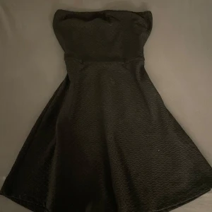 Svart axelbandslös vintage klänning - Elegant svart axelbandslös klänning med en klassisk och tidlös design. Perfekt för festliga tillfällen. Klänningen har en smickrande passform och en lätt utsvängd kjol. Passar M/S/XS
