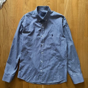 Rutig skjorta från Polo Ralph Lauren - Snygg rutig skjorta från Polo Ralph Lauren i blått och vitt. Skjortan har en klassisk krage och knappar framtill. Den är slim fit och har långa ärmar. Perfekt för en stilren look.