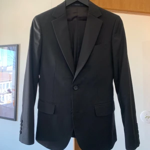 Svart kavaj herr - Säljer en klassisk svart kavaj med smal passform. Kavajen har två knappar framtill, fickor med lock och knappar vid ärmslut. Perfekt till student, bal eller fest. Passar dig som vill ha en stilren och tidlös look.