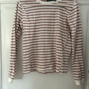 Randigt sett från Pieces - Säljer en långärmad tröja från Pieces i vitt och ljusrosa med horisontella ränder. Tröjan har rund halsringning och är tillverkad i mjuk bomull, perfekt för en avslappnad stil. Med matchande byxor till.