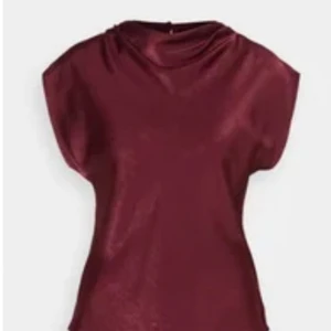 Vinröd satintopp med draperad hals - Säljer en elegant vinröd topp i satin med draperad halsringning och korta ärmar. Perfekt för dig som vill ha en stilren och trendig look. Toppen har en mjuk glans och ett lyxigt fall.