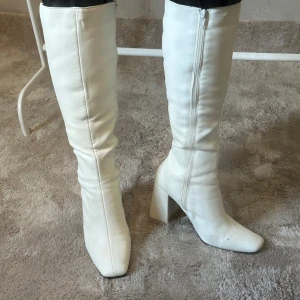 Vita boots med klack från Public Desire  - Säljer ett par vita höga boots från Public Desire med bred klack och rund tå. Skorna har dragkedja på insidan.  Klacken är 10 cm. Har använts några gånger och har därav skråmor och platser där färgen försvunnit. Går fortfarande att bära de utan problem. Alla defekter syns på bilden. 