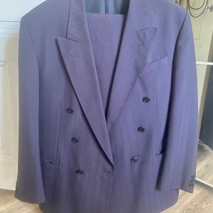 Dubbelknäppt kostym 80-tal - En riktigt snygg dubbelknäppt kostym från 80-talet av märket Licona. Rymlig och lös i passformen precis som den ska vara. Färgen på kostymen är en väldigt mörk lila.