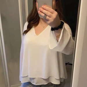 Vit blus med v-ringning från KappAhl - Säljer en vit blus från KappAhl med v-ringning och långa, vida ärmar. Blusen har en lös passform och är tillverkad i ett lätt och luftigt material, perfekt för vår och sommar.