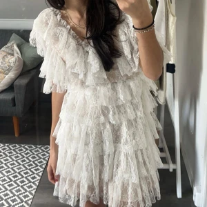  By Malina klänning. Vit spetsklänning med volanger  - Superfin vit kortklänning i spets med flera lager volanger och v-ringning. Klänningen har korta ärmar och romantisk känsla, perfekt för speciella tillfällen. Säljer då den inte kommer till användning längre. Använd en gång. Som ny inga skador. Syns inte att den är använd