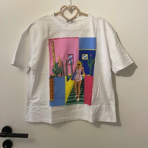 T-shirt från zara - Vit t-shirt med ett stort, färgglatt tryck framtill. T-shirten har rund hals och korta ärmar. Perfekt för dig som gillar unika motiv och streetstyle.