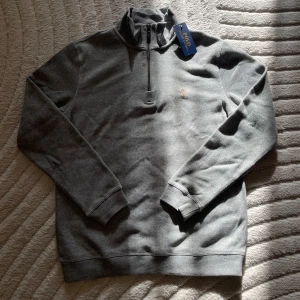 Polo Ralph Lauren sweatshirt - Säljer en stilren grå sweatshirt från Polo Ralph Lauren med halv dragkedja och klassisk broderad logga på bröstet. Perfekt för en avslappnad och snygg look.